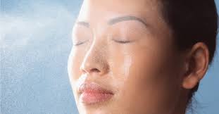 Smiling woman misting water on face – refreshing hydration moment representing benefits of MD Ultimate Moisturizer for dry, sensitive skin