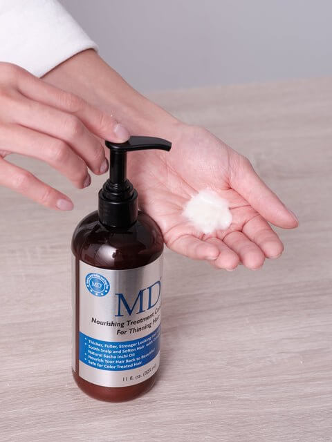 Lifestyle photo of MD® Revitalizing Treatment Conditioner being pumped into hand – nutrient-rich formula for thinning hair, scalp hydration, and hair repair, part of the MD Hair system